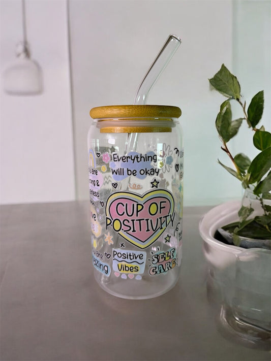 Gourde en verre "Cup of positivity". D'autres textes en anglais sont inscrits avec des cœurs et des étoiles.
La gourde possède un couvercle en bois et une paille en verre.