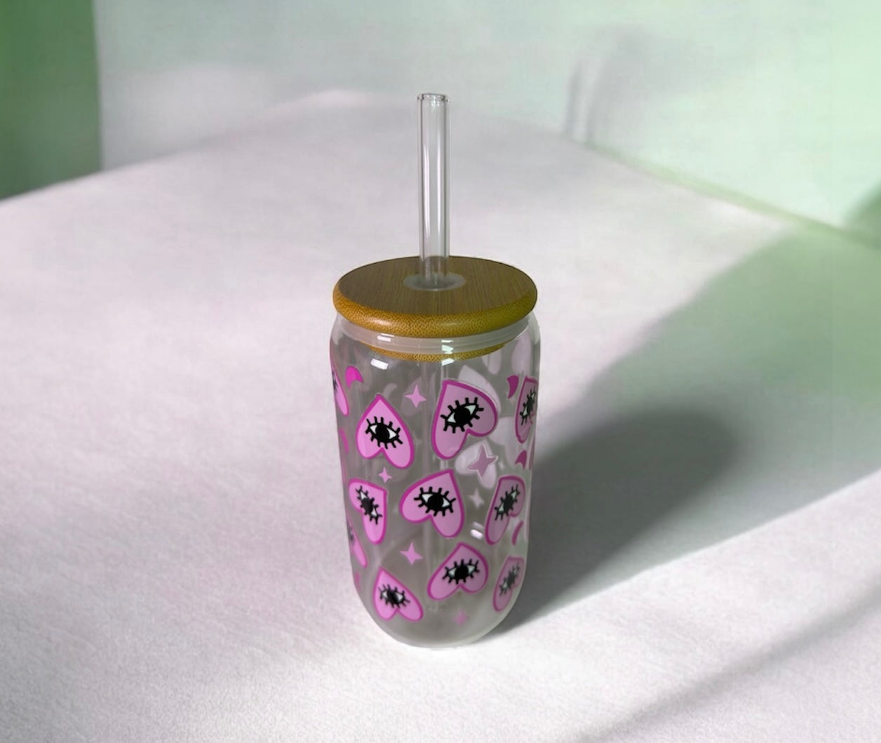 Vue de profil pour une gourde en verre avec un flocage coeur rose, oeil et étoiles. Le bouchon est en bois et la paille en verre.