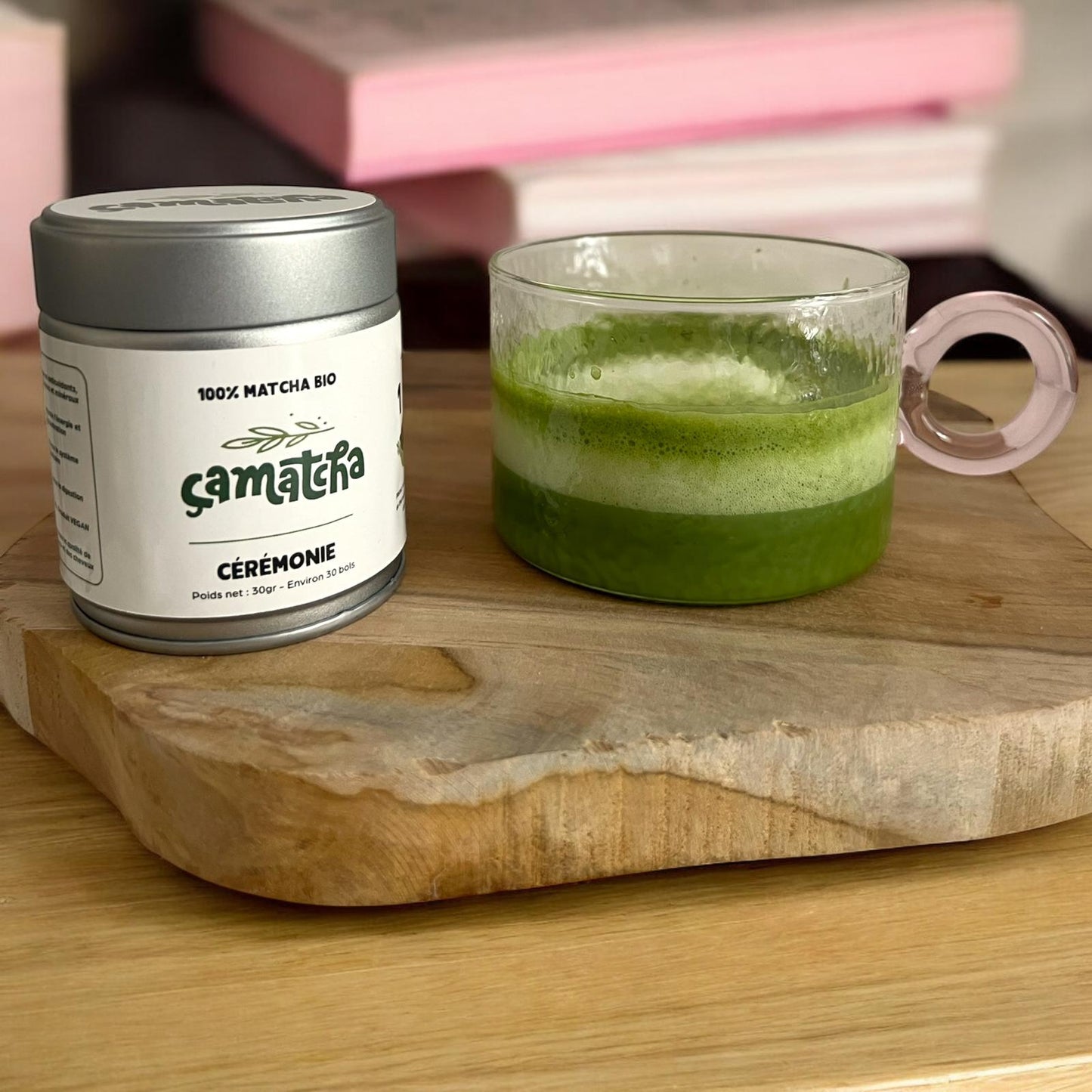 Présentation d'un moment matcha. On retrouve un pot de poudre matcha qualité cérémonie ainsi qu'un tasse de matcha prête à être déguster. Les deux sont posés sur une épaisse planche en bois.
